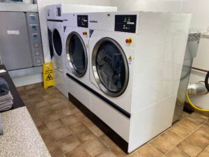 A photograph of a row of 3 white dryers in a laundry room