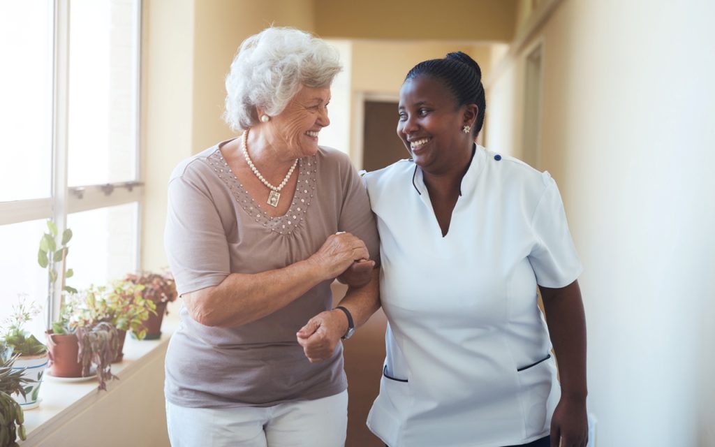 A happy female caregiver and senior woman walking together